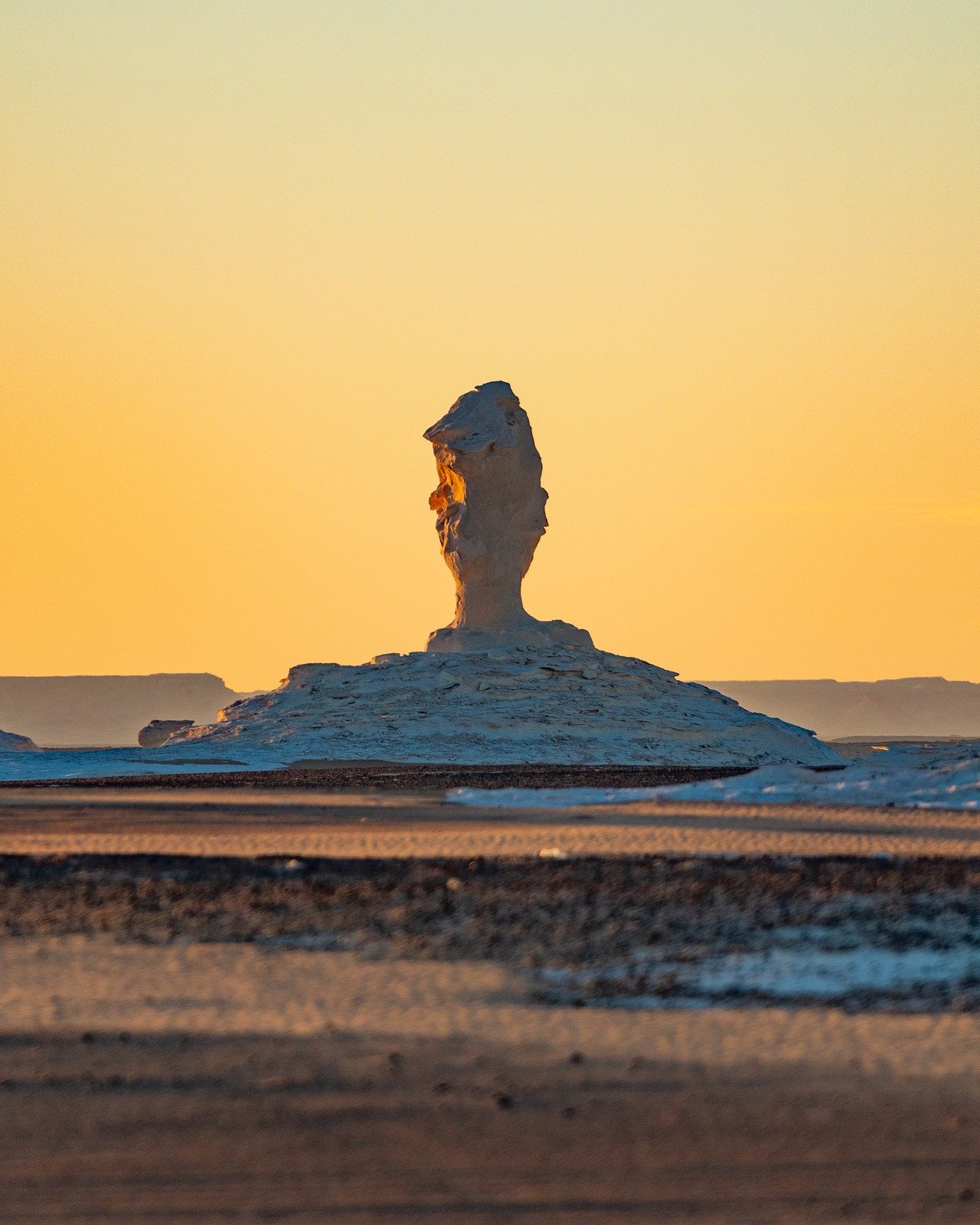A lone rock pillar silhouetted against an orange desert sunset
