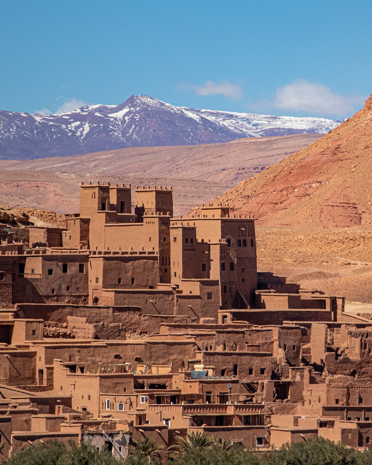 A mud-brick kasbah on a hillside below snow-capped mountains